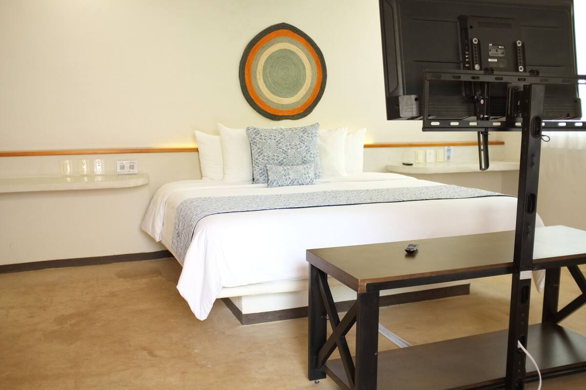 Ein Hotelzimmer mit einem Bett, einem Nachttisch, einem an der Wand montierten Fernseher und einem Ablagefach mit Toilettenartikeln.