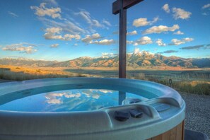 Un bain à remous doté d’une structure en bois, installé dans un paysage montagneux sous un ciel dégagé.
