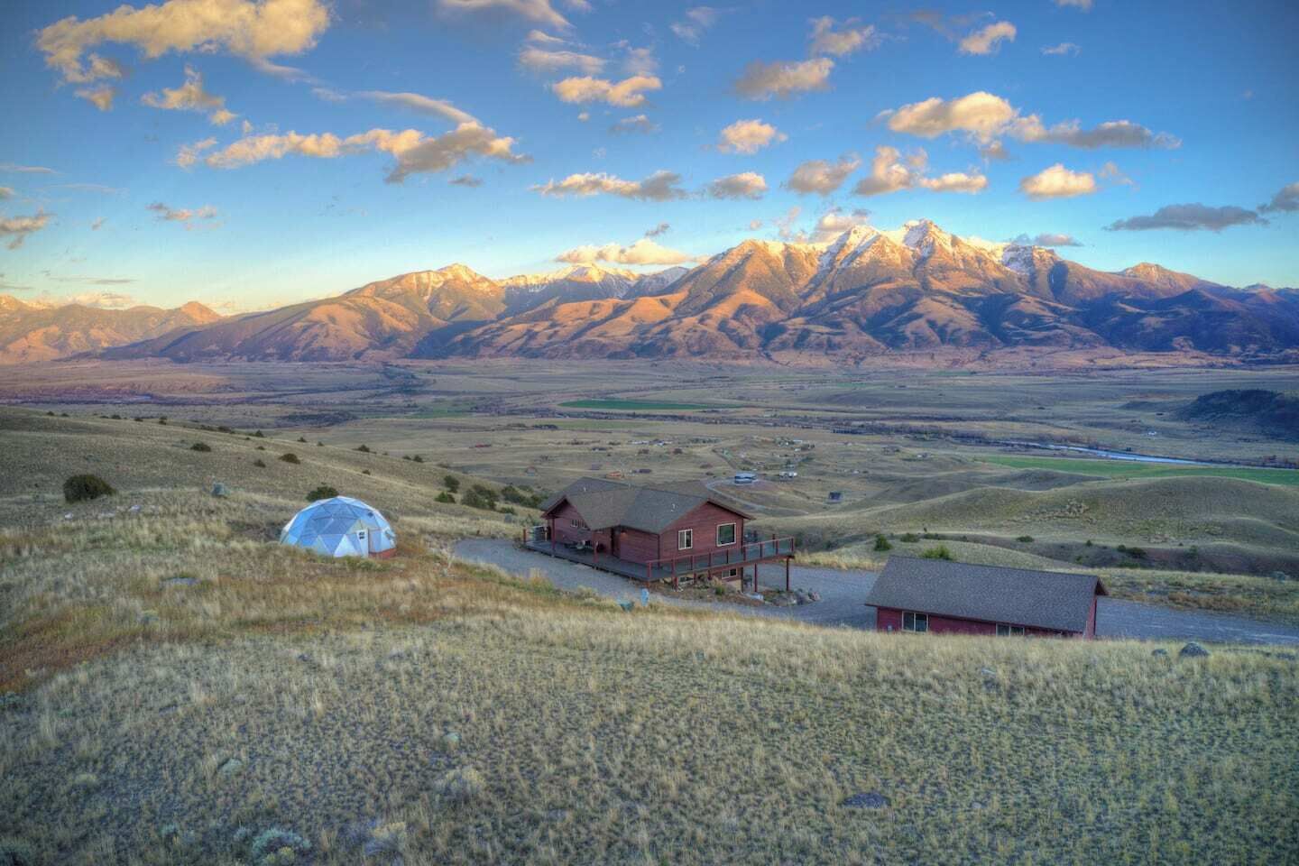 A rural landscape with a house, a small shed, and a dome tent.