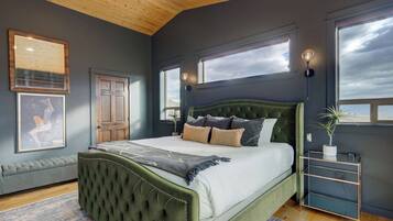 A bedroom with a green upholstered bed, a bench, a bedside table, and a large window.
