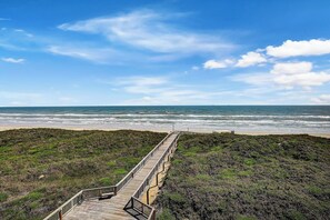 A wooden boardwalk leading to a beach with a clear sky.