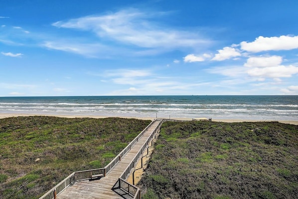 A wooden boardwalk leading to a beach with a clear sky.