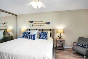 A hotel room with a bed, bedside tables, a chair, and a ceiling fan.