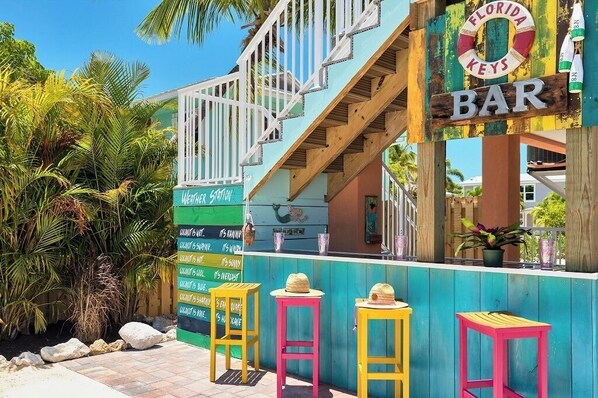 A colorful bar with a wooden staircase, outdoor seating, and a sign indicating it is in the Florida Keys.