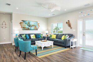 A living room with a gray sofa, teal chairs, a white coffee table, and a colorful rug.