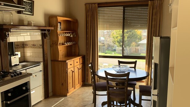 Une cuisine avec un plafond en bois, une table à manger avec des chaises, un réfrigérateur et une fenêtre avec des stores.