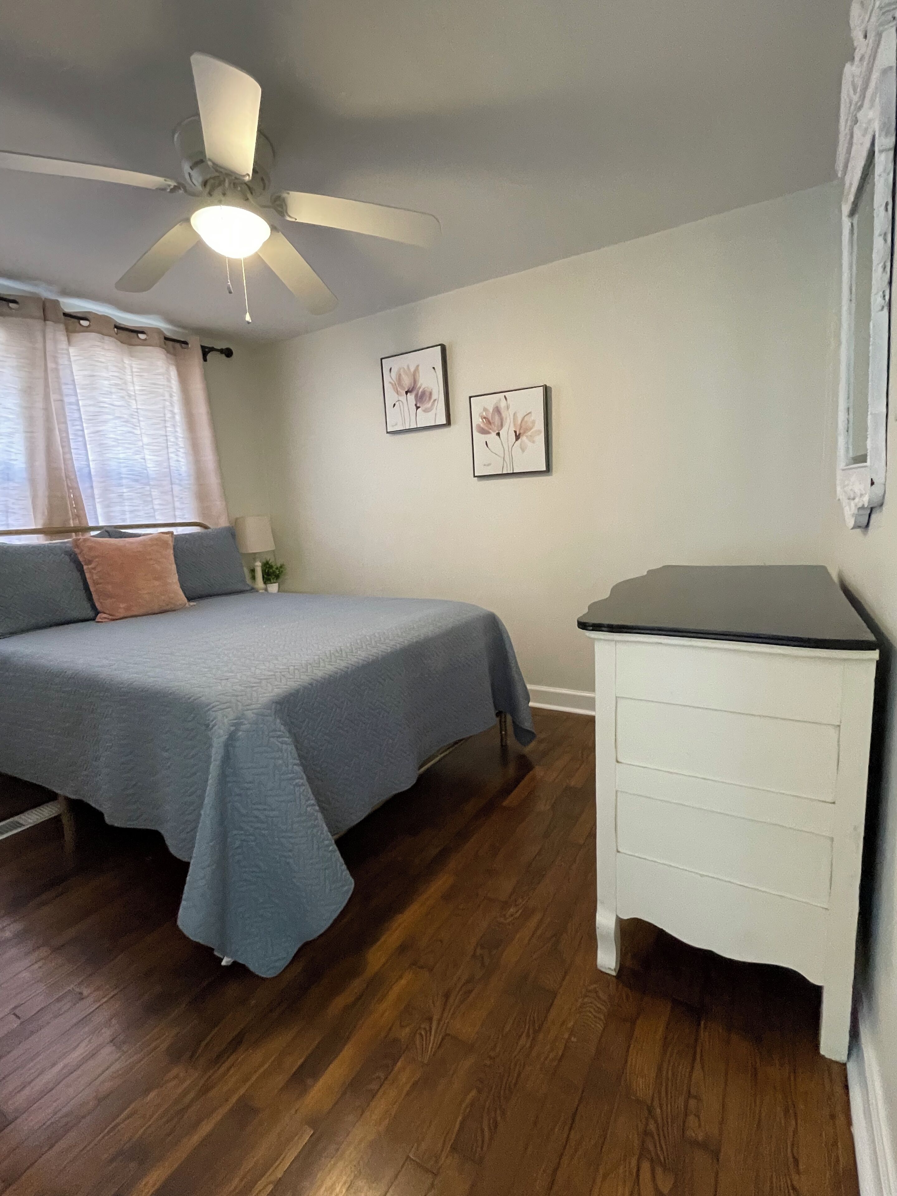 A bedroom with a bed, a nightstand, a ceiling fan, and two wall-mounted pictures.