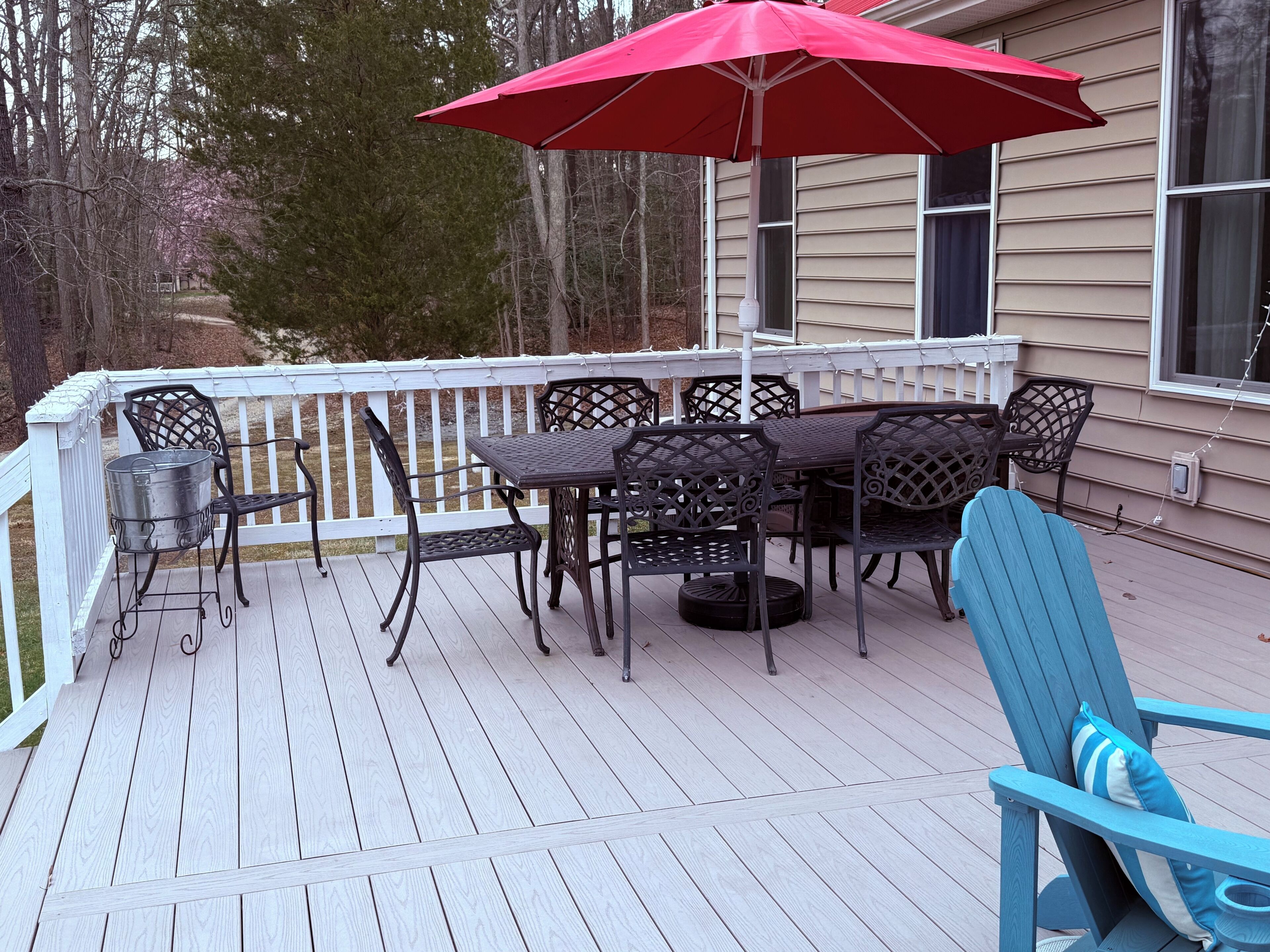 Une terrasse en bois avec une table et des chaises, un parasol rouge et une chaise bleue.