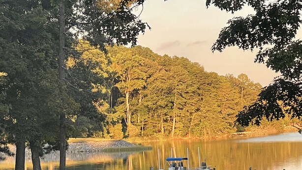 Eine Seenlandschaft mit Steg, Boot und roten Adirondack-Stühlen im Gras.
