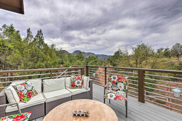 An outdoor deck with wicker furniture and a round table, overlooking a mountainous landscape.