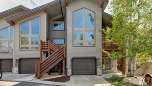Un immeuble résidentiel à plusieurs étages, doté d’un garage, d’un escalier et d’un arbre dans le jardin avant.