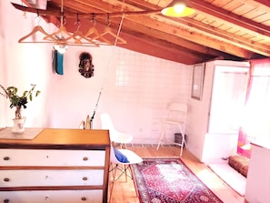 A room with a wooden ceiling, a white chair, a patterned rug, and a dresser with drawers. - Sandomil Riverbeach Tiny House (Sandomil)