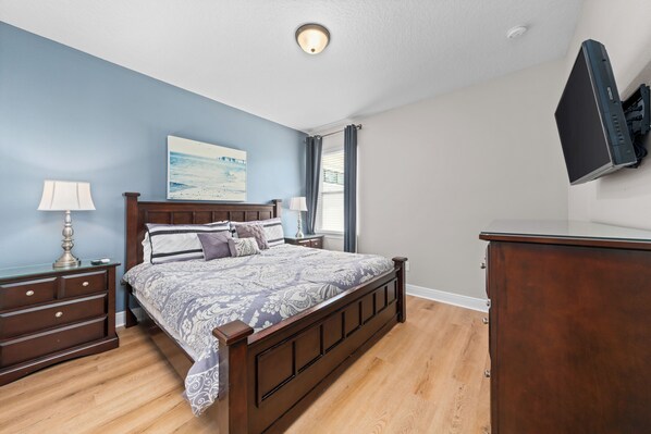 A bedroom with a wooden bed, a nightstand, a dresser, and a flat-screen TV mounted on the wall.