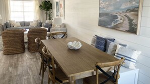 Un comedor con una mesa y sillas de madera, un conjunto de sofás y un cuadro de una playa.