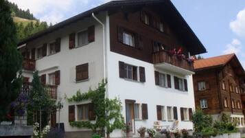 Ein mehrstöckiges Gebäude mit weißer Fassade und braunen Fensterläden, mit Balkonen, die mit Pflanzen und Blumen geschmückt sind.