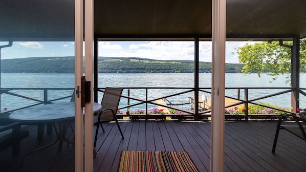Une terrasse avec vue sur un lac et des collines, une chaise, une table et une rambarde.