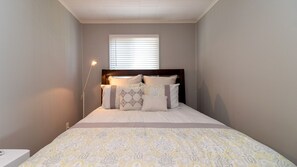 Une chambre à coucher avec un lit, une table de chevet, une lampe et une fenêtre avec des stores.