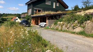 Une maison à deux étages, avec un toit en pente, un porche couvert et une voiture garée devant.