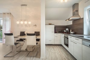 A modern kitchen with white cabinets, a stainless steel range hood, and a dining area with a table and chairs.