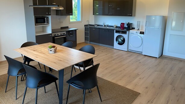 Una cocina moderna con comedor, que incluye una mesa y sillas de madera, microondas, horno, lavadora y refrigerador.