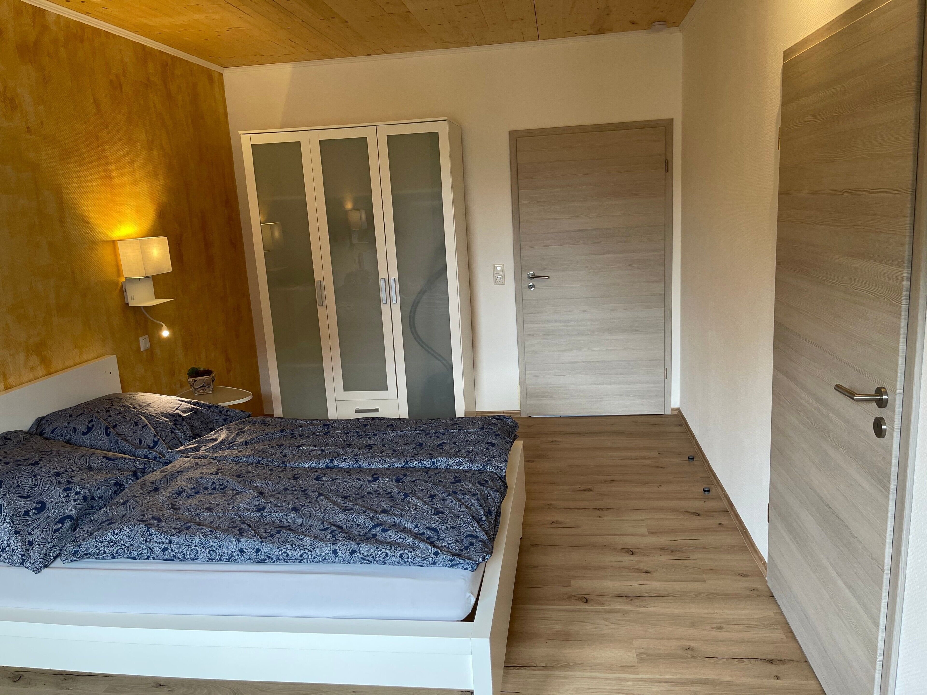 Een slaapkamer met een bed, een kledingkast, een nachtkastje en een lamp.
