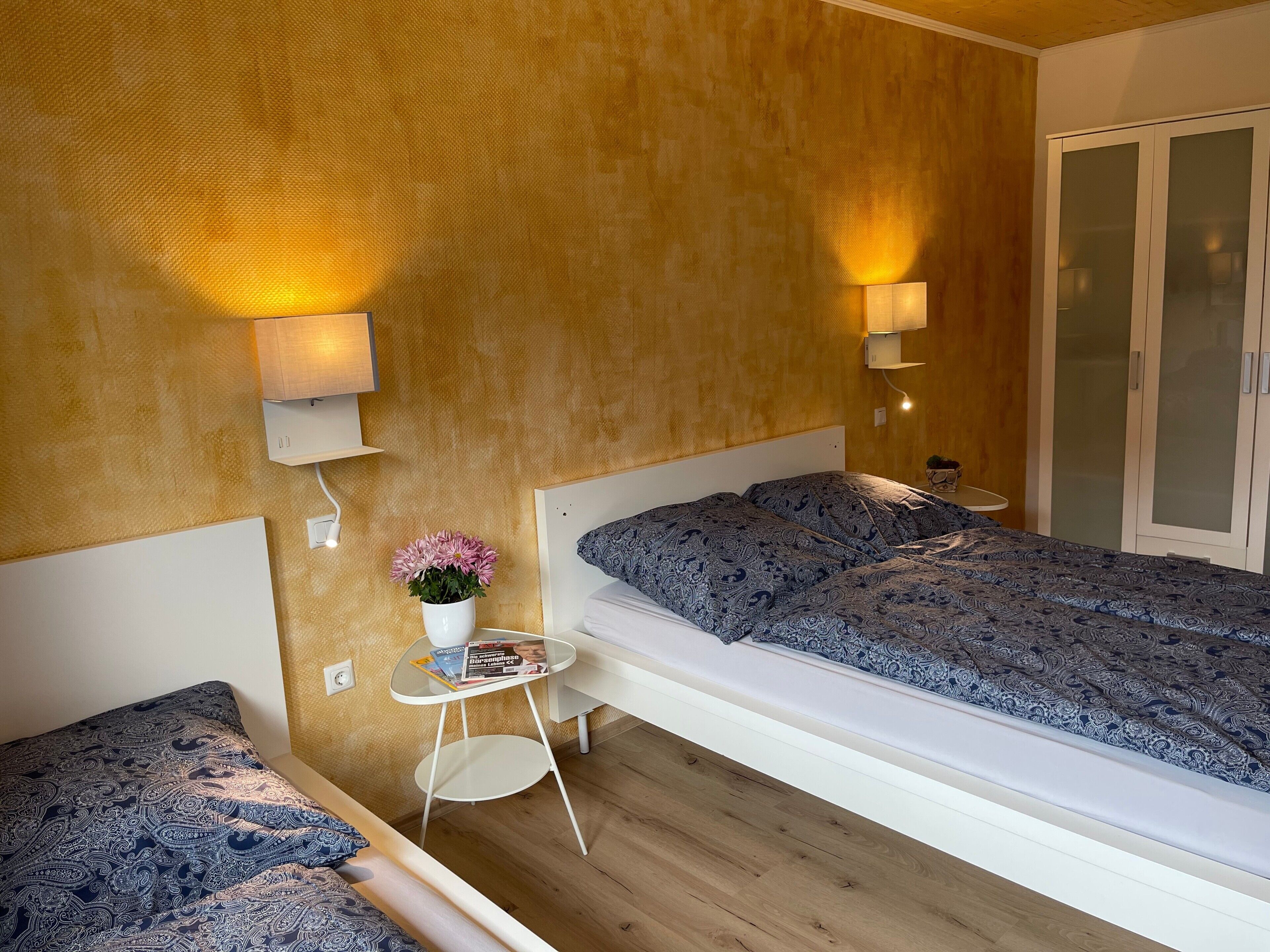 A modern bedroom with a bed, bedside tables, a small desk, and a wall-mounted lamp.