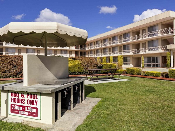 A hotel with a BBQ and pool area, a covered picnic table, and a sign indicating BBQ & pool hours.