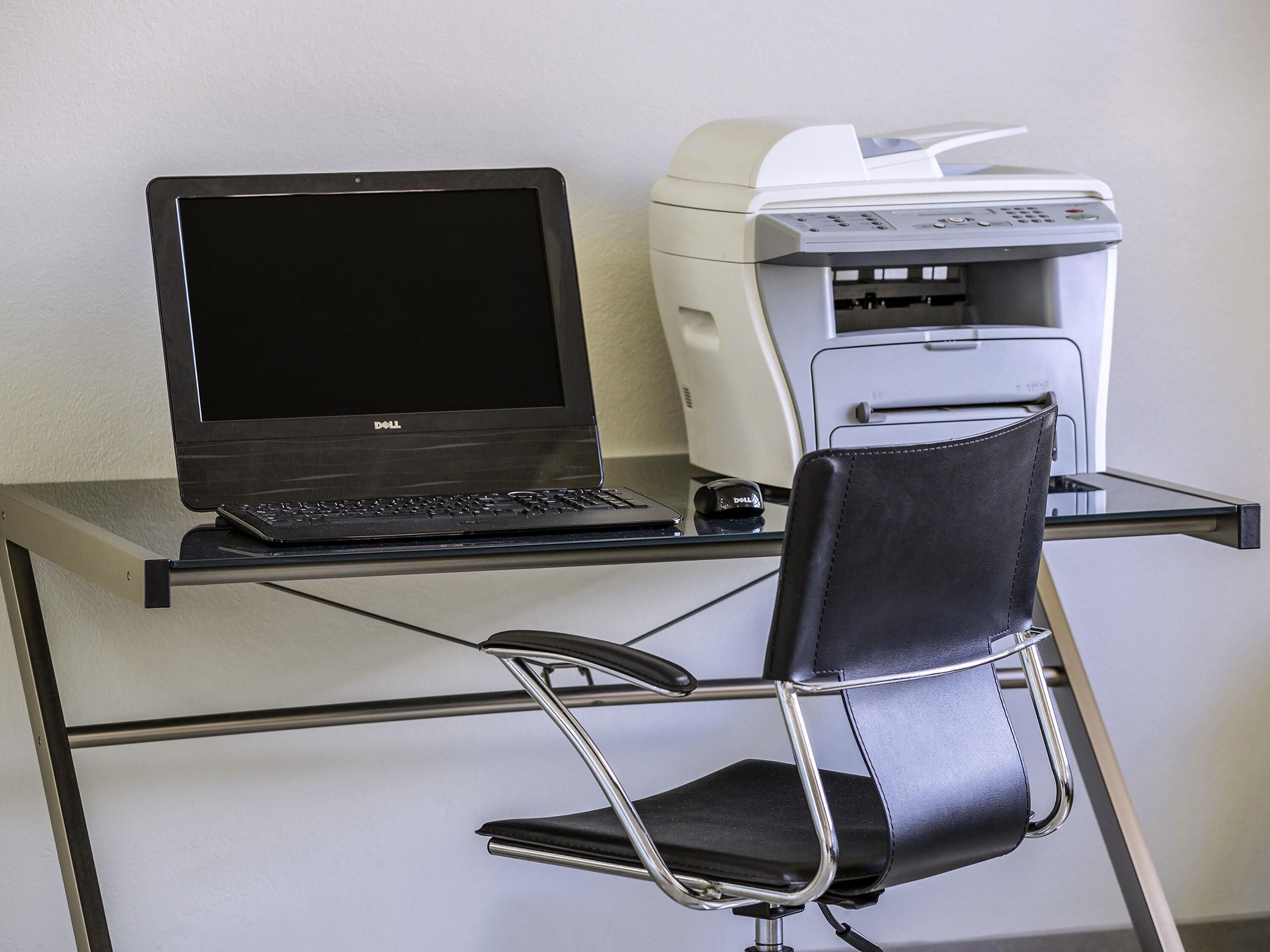 A laptop on a glass desk, a printer, and a black chair.