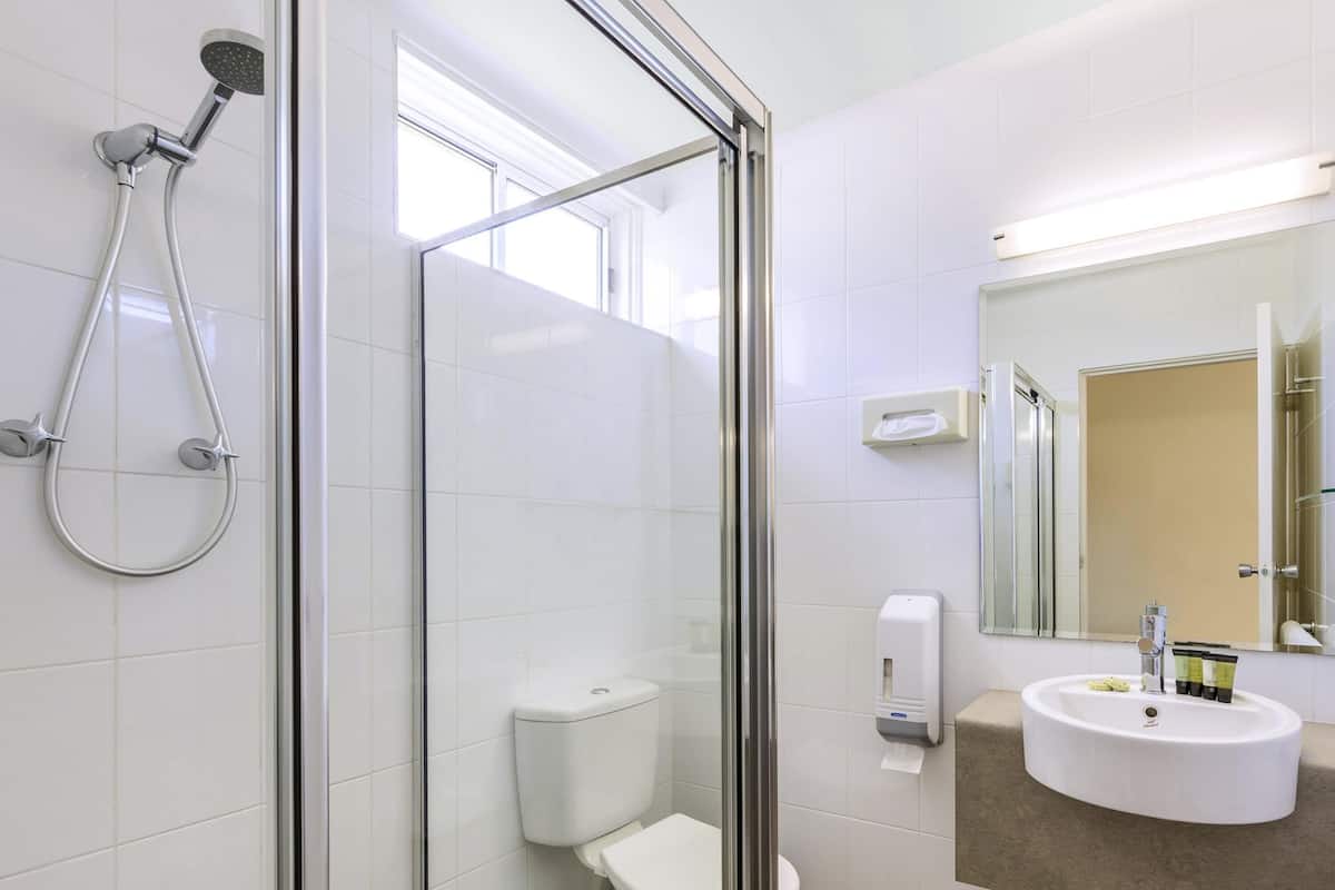 A modern bathroom with a glass-enclosed shower, a toilet, a sink with toiletries, and a mirror.