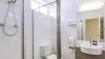 A modern bathroom with a glass-enclosed shower, a toilet, a sink with toiletries, and a mirror.