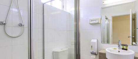 Un baño moderno con ducha envuelta en vidrio, inodoro, lavamanos con artículos de aseo y espejo.