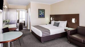 Ein Hotelzimmer mit Bett, Schreibtisch, Stuhl, einer Couch und einem Bild an der Wand.