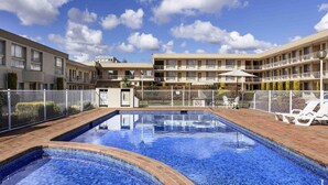 Ein Hotel mit Schwimmbad, mehreren Balkonen und blauem Himmel.