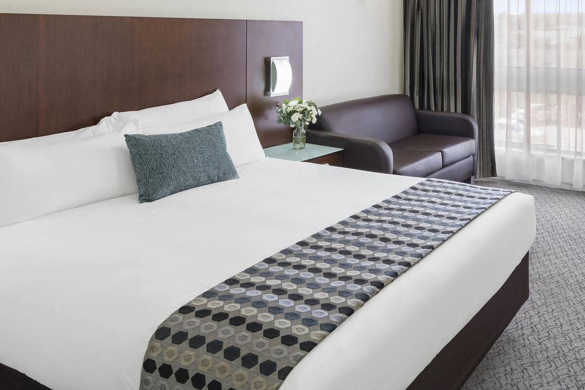 A hotel room with a large bed, a nightstand, a chair, and a window with curtains.