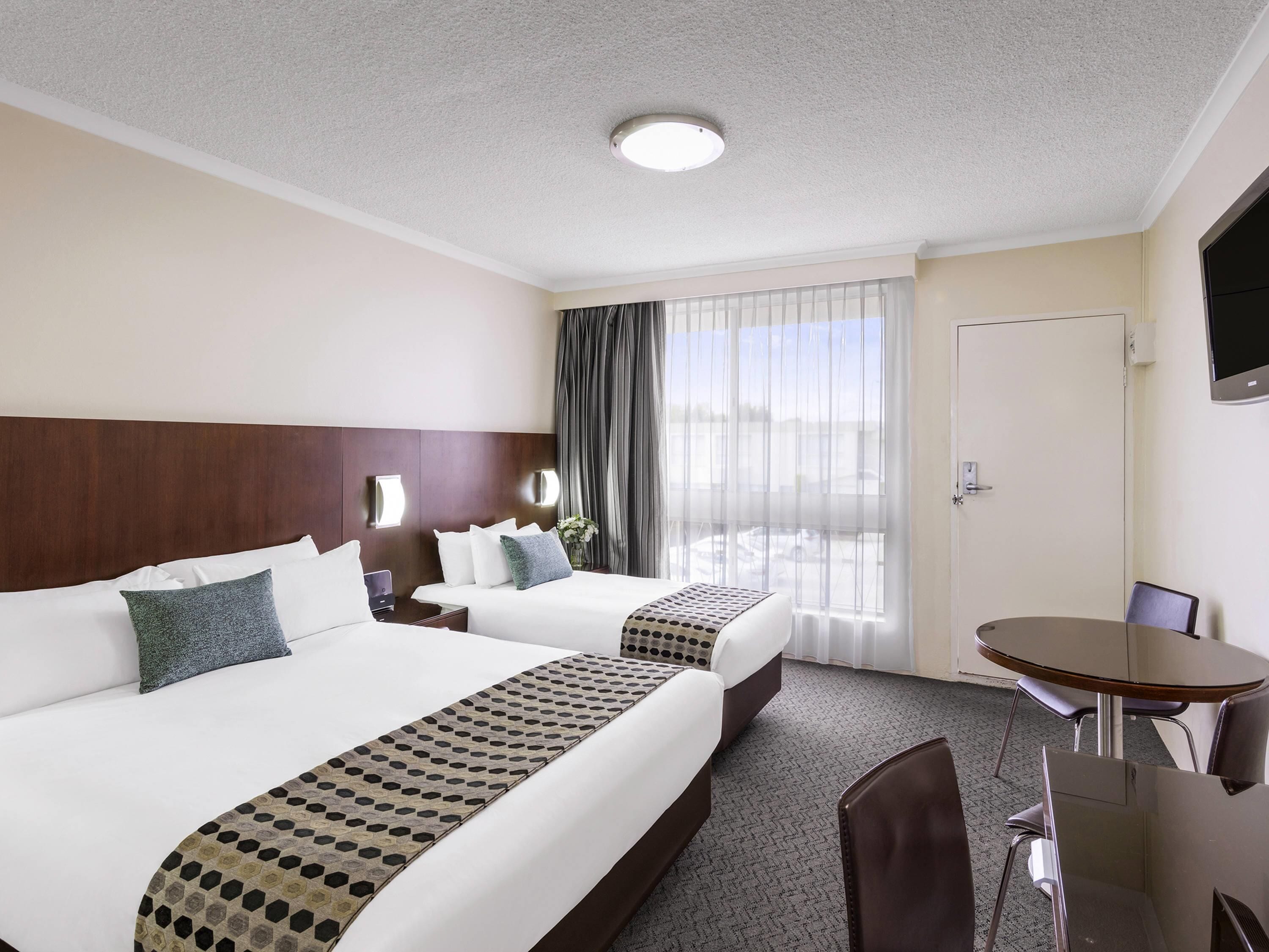 Une chambre d’hôtel avec deux lits, une table à manger, un téléviseur et une fenêtre avec des rideaux.