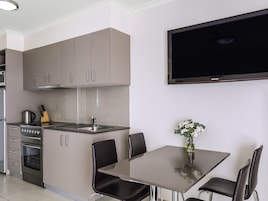 Una cocina moderna con gabinetes grises, horno empotrado, estufa y pileta. Se observa una mesa de comedor con sillas y un televisor de pantalla plana montado en la pared.
