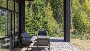 Une terrasse couverte avec deux canapés et une table, donnant sur une forêt.