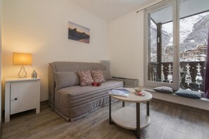 Een knus interieur met een bank, een klein tafeltje, een lamp en een raam met uitzicht op besneeuwde bergen.