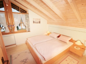 Ein Schlafzimmer mit Holzboden, einem Bett mit rosa Bettwäsche, einem Nachttisch mit Lampe und einem Fenster mit Vorhängen.