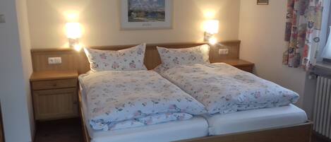 A double bed with floral bedding, two bedside lamps, a nightstand, a framed picture on the wall, and a radiator.