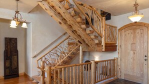 Una escalera de madera con barandilla, una puerta con panel decorativo y un candelabro.