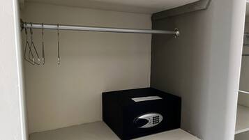 Una caja de almacenamiento con candado sobre un estante blanco en una habitación con pared gris y una barra metálica.