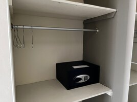 Una caja de almacenamiento con candado sobre un estante blanco en una habitación con pared gris y una barra metálica.