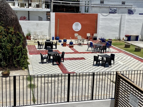 Un patio al aire libre con mesas y sillas, suelo a cuadros y un cartel que indica un enchufe.