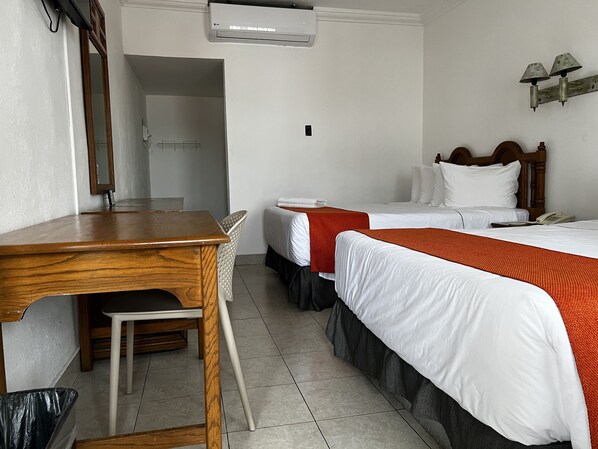 Una habitación de hotel con dos camas, un escritorio de madera, una silla y un cesto de basura.