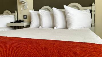 A hotel room with a bed, white pillows, a white headboard, a nightstand with a phone, and a red blanket.