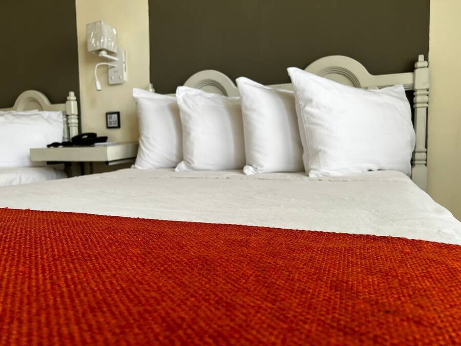 A hotel room with a bed, white pillows, a white headboard, a nightstand with a phone, and a red blanket.