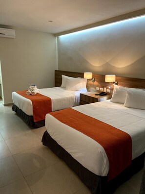 Habitación de hotel con dos camas, cada una con ropa blanca y mantas naranjas. Hay dos mesitas de noche con lámparas y un teléfono.