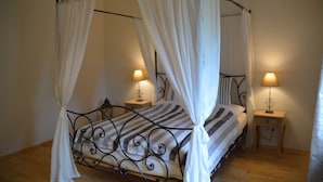Una cama con dosel, cortinas blancas, dos mesitas de noche con lámparas y suelo de madera.