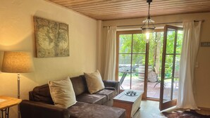 Una sala de estar acogedora con un sofá seccional marrón, una mesa de centro de madera, una lámpara, un mapa mundial en la pared y un ventanal con vistas al exterior.